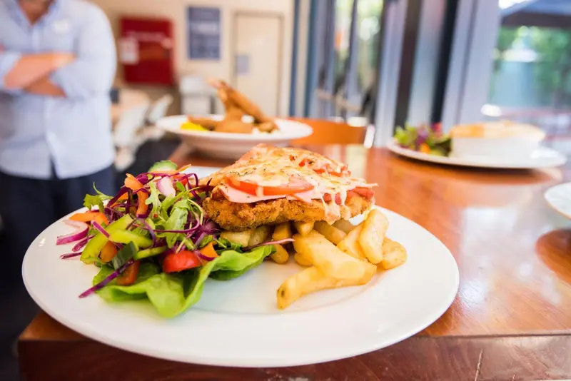 Une assiette généreuse de frites, de salade et d'un plat pané garni de tomates est mise en valeur sur une table en bois.