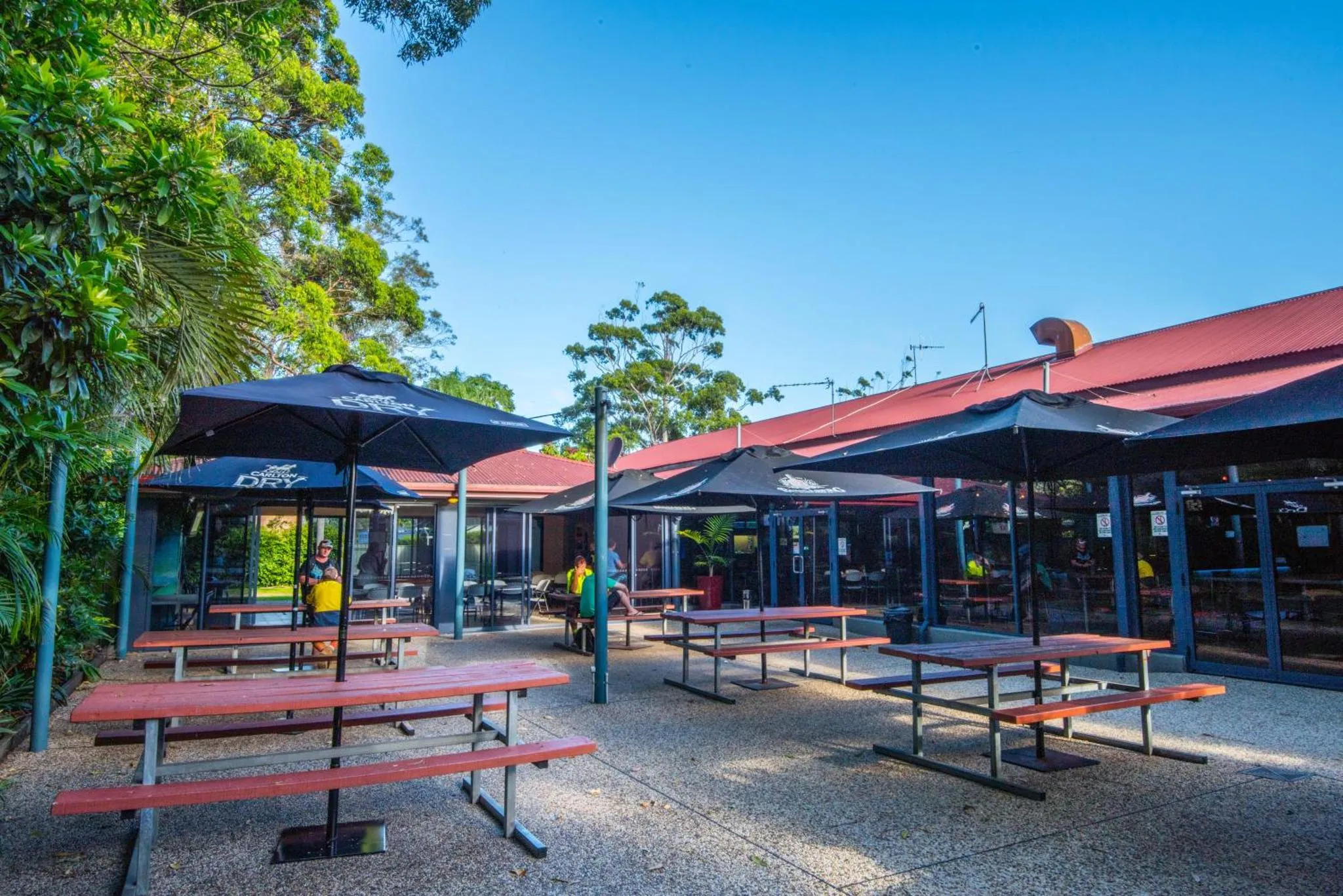 Terrasse ombragée avec tables et parasols devant un bâtiment.