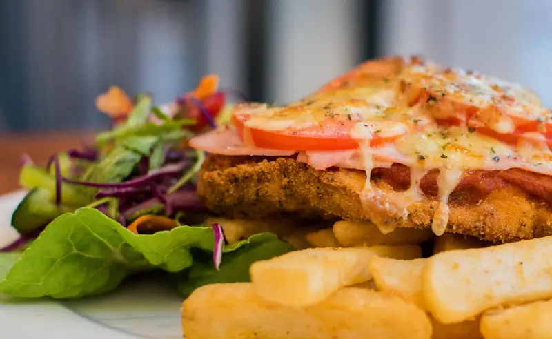 Assiette généreuse composée d'une escalope panée gratinée, de frites et d'une salade colorée.