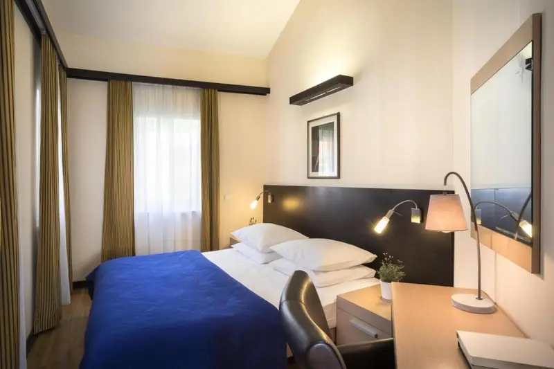 Une chambre d'hôtel lumineuse avec un lit bleu et un bureau.
