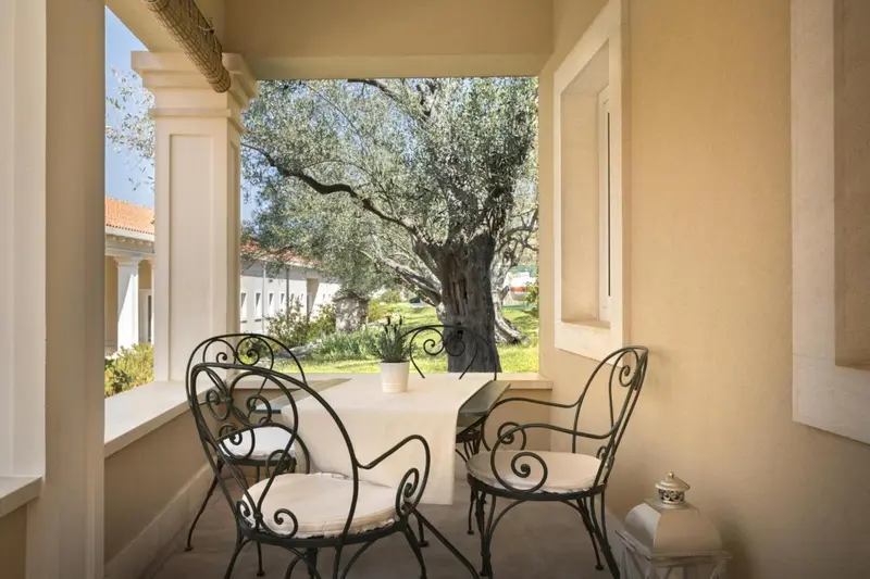 Terrasse ombragée avec mobilier en fer forgé donnant sur un jardin verdoyant.