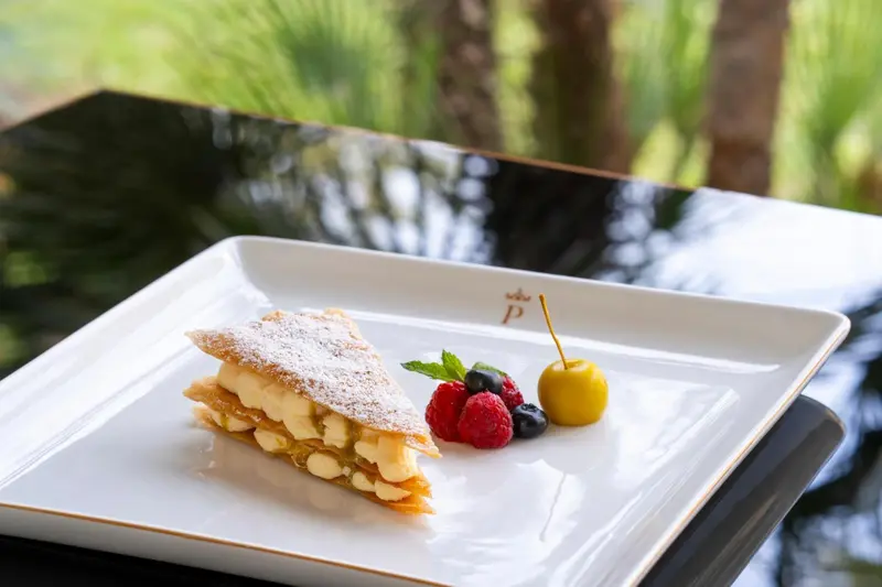 Une part de gâteau à la crème, décorée de fruits rouges et d'une feuille de menthe, est présentée sur une assiette blanche.