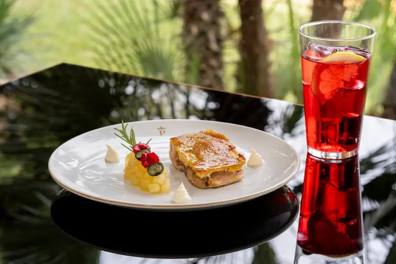 Assiette de plat raffiné avec une boisson rouge sur une table sombre.