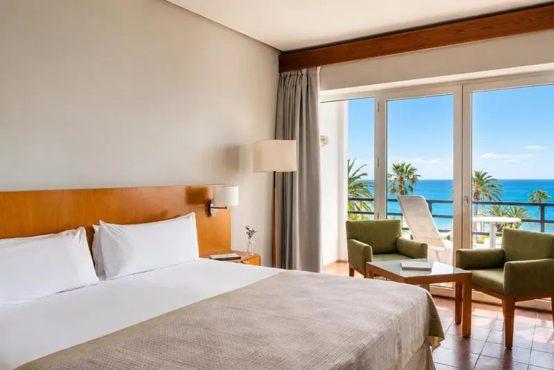 Une chambre lumineuse avec un grand lit donnant sur une vue mer.