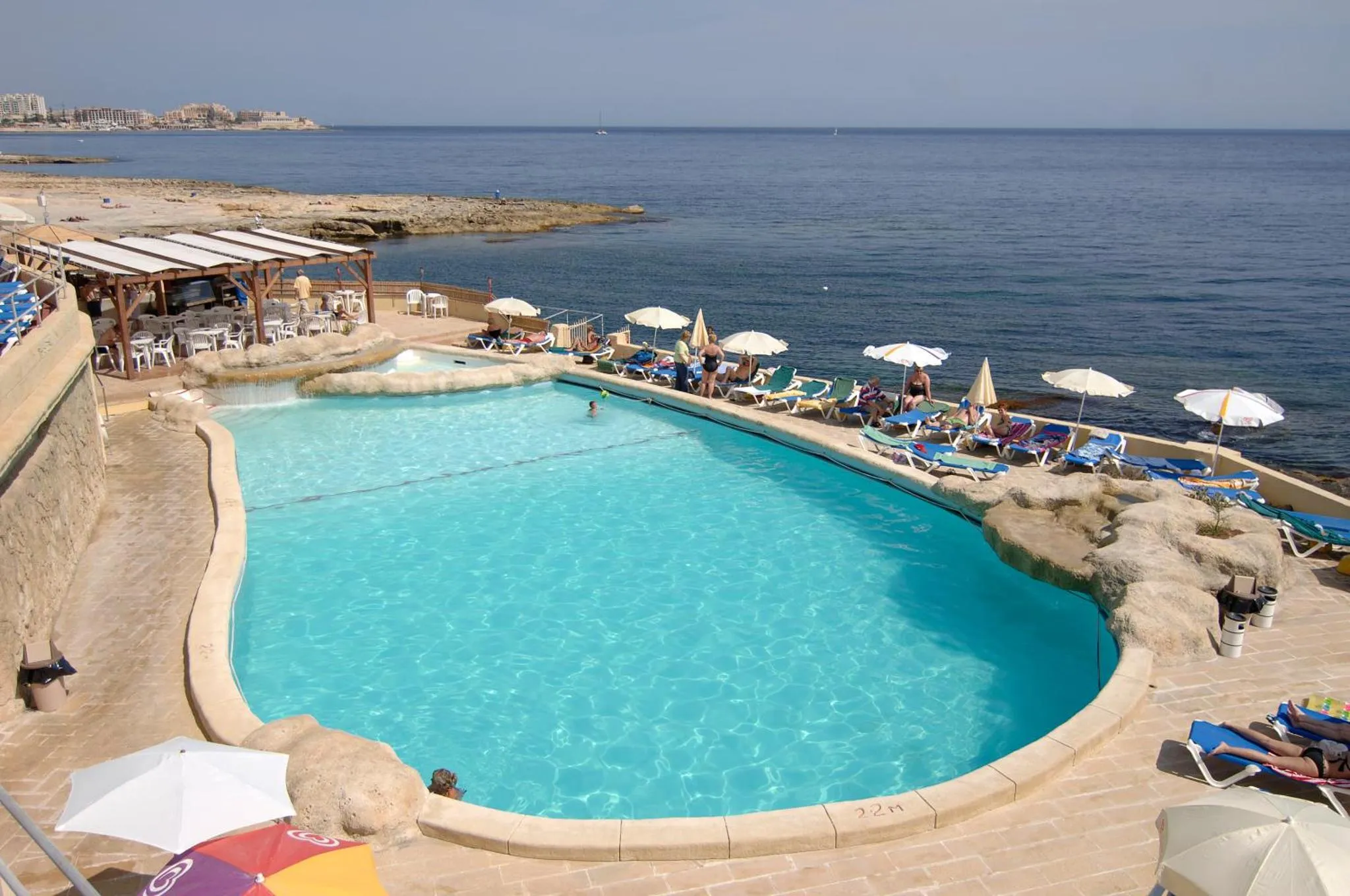 Une piscine turquoise bordée de transats et de parasols, avec une vue sur la mer.