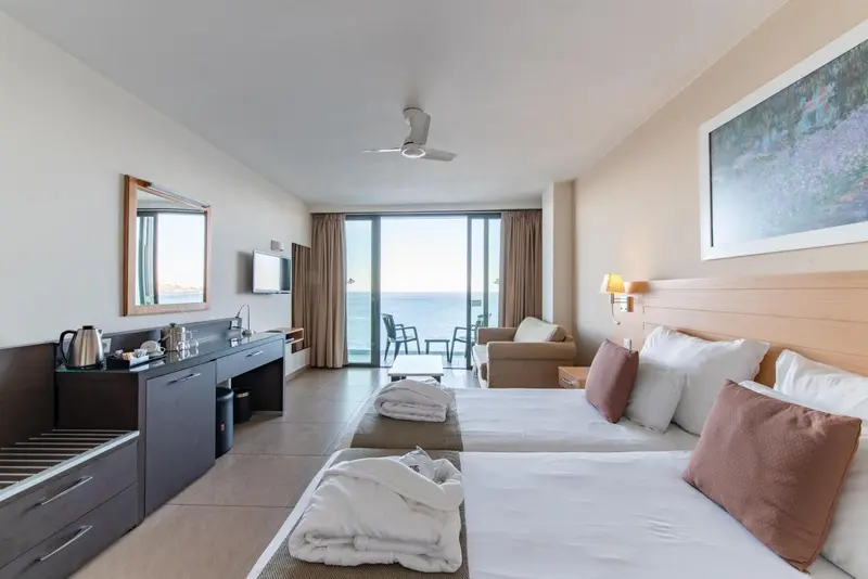 Une chambre lumineuse avec un lit double et un coin salon donnant sur la mer.
