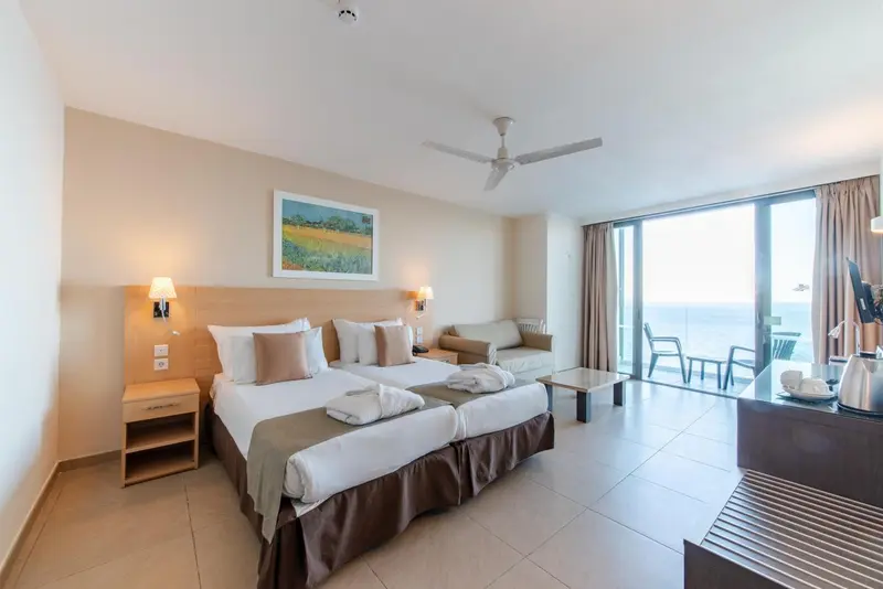 Chambre lumineuse avec un lit double et un coin salon donnant sur une vue mer.