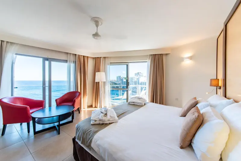 Chambre lumineuse avec un lit double et un accès à un balcon offrant une vue sur la mer.