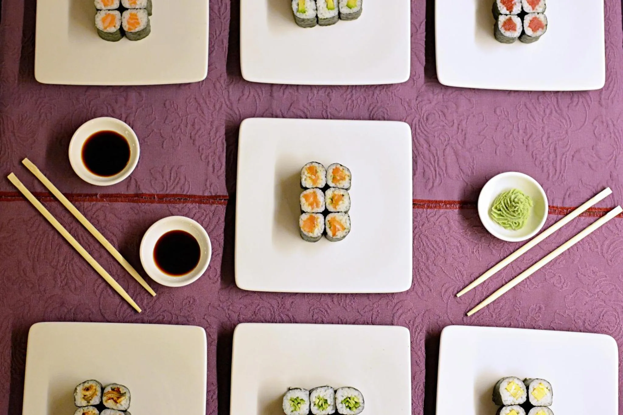 Assortiment de sushis présentés sur des assiettes blanches et une nappe violette.