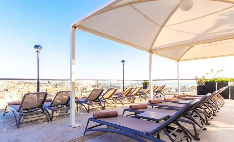 Terrasse aménagée avec des transats et une vue sur la ville et la mer.