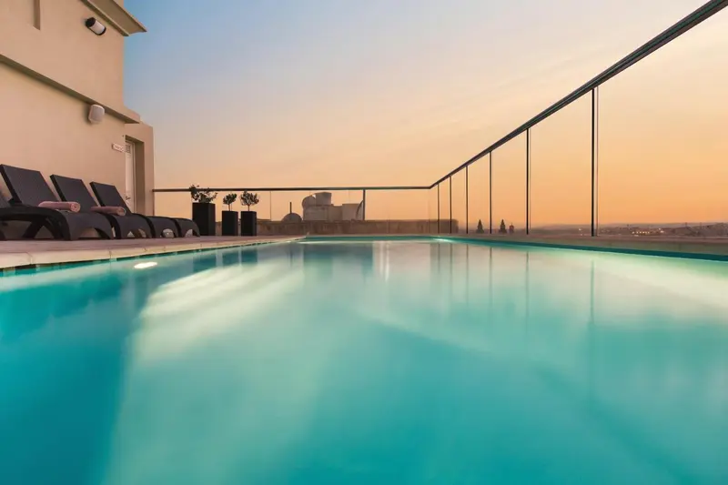 Une piscine turquoise reflète les couleurs d'un ciel orangé au coucher du soleil.