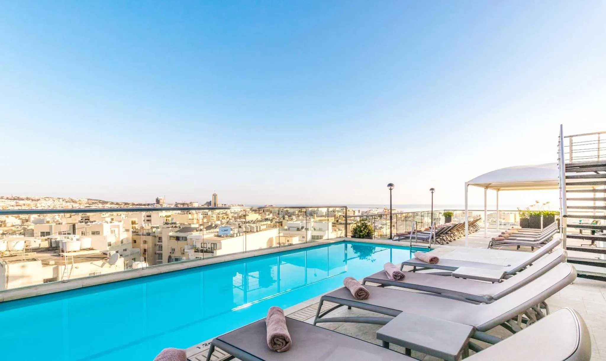 Transats alignés au bord d'une piscine à débordement avec vue sur la ville et la mer.