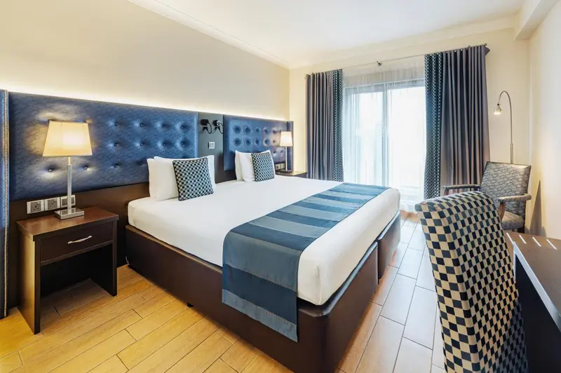 Chambre lumineuse avec un grand lit et un fauteuil.