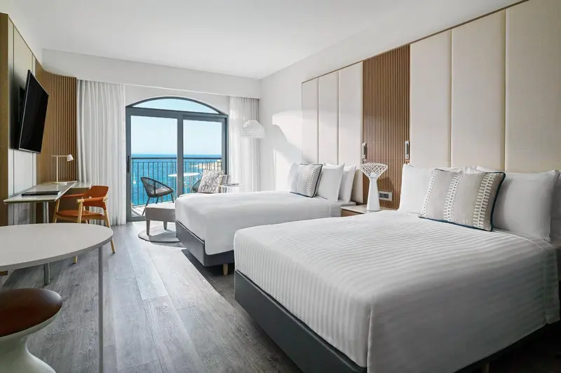 Chambre lumineuse avec deux lits et vue sur la mer.