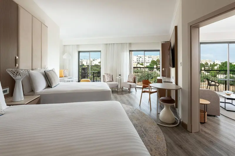 Chambre lumineuse avec un grand lit et un espace détente donnant sur une vue extérieure.