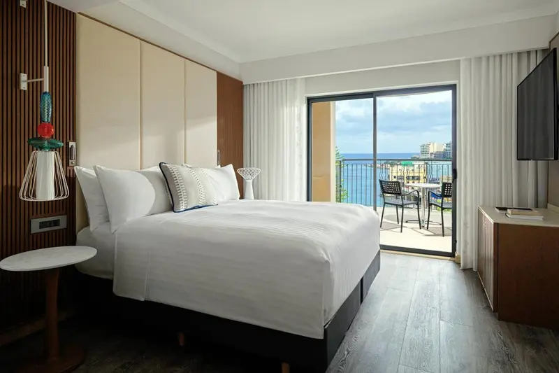 Une chambre lumineuse avec un grand lit et un accès à un balcon avec vue sur la mer.