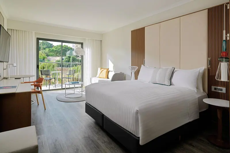 Une chambre lumineuse avec un grand lit et un coin salon donnant sur une terrasse.