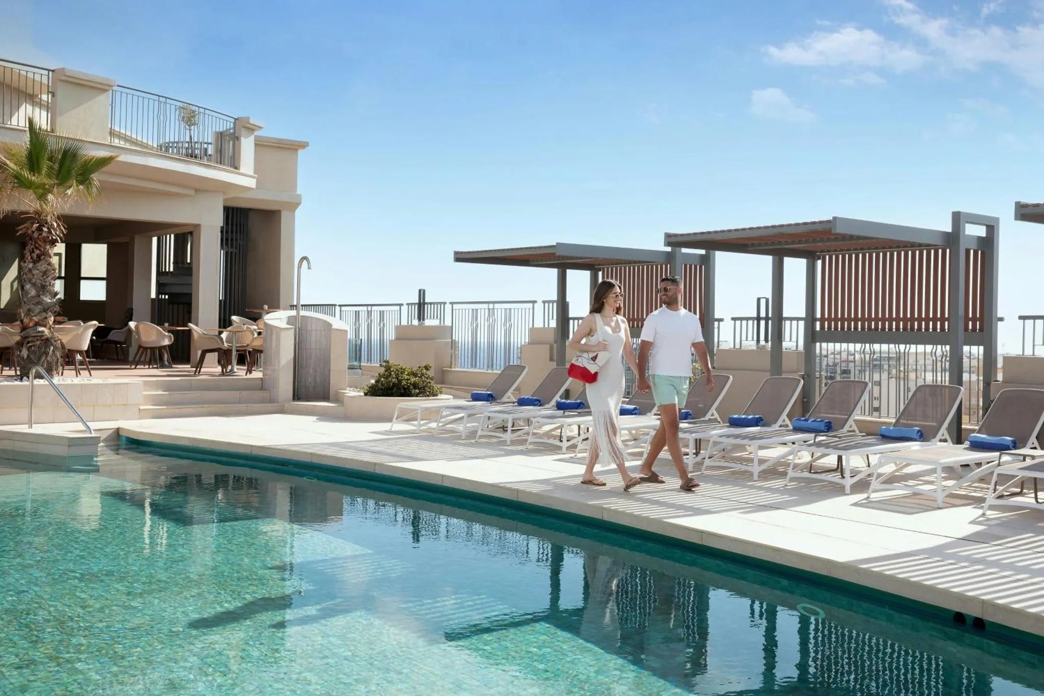 Une piscine bordée de transats avec des personnes se promenant sur une terrasse.