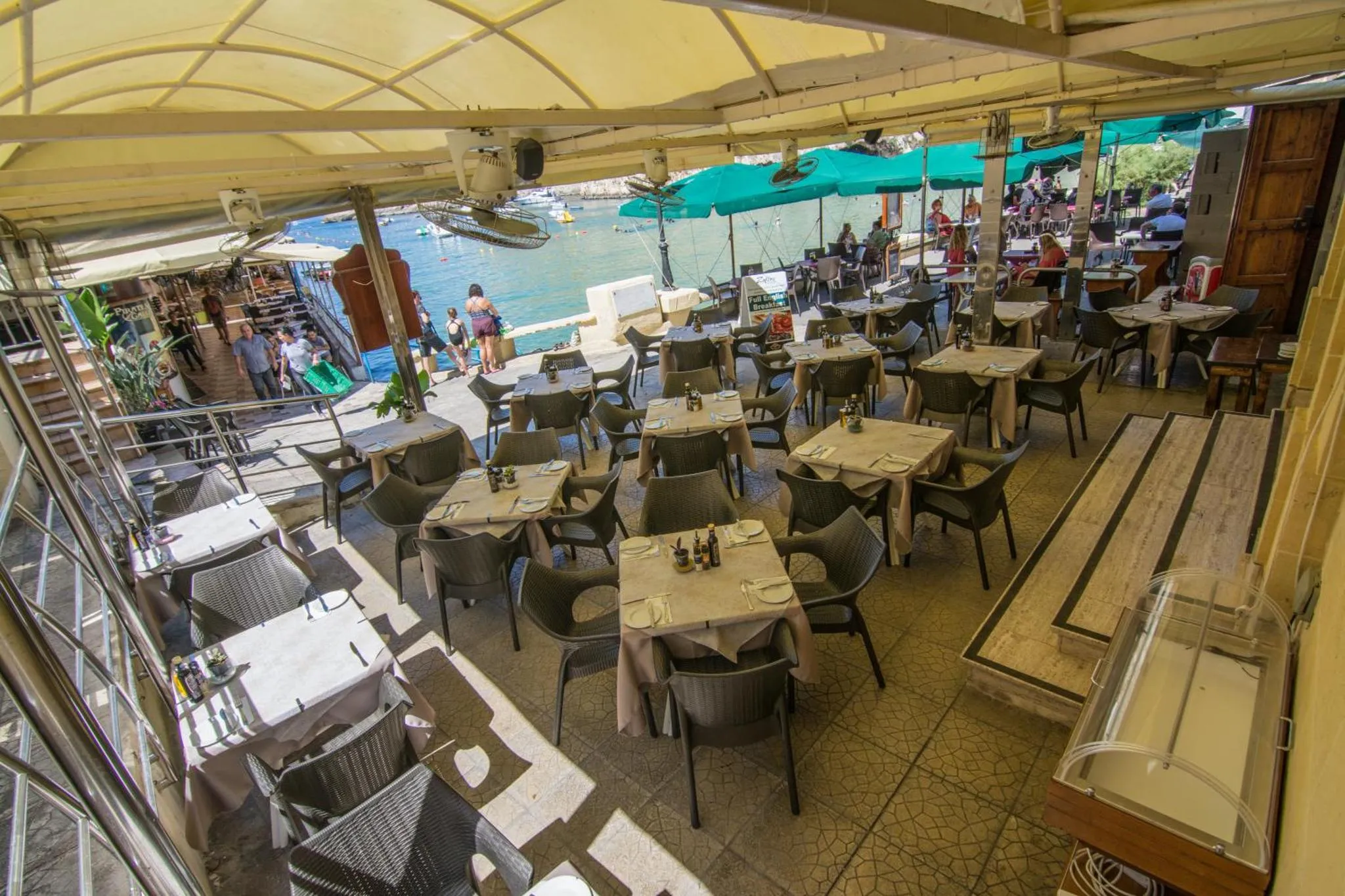 Terrasse ombragée avec tables et chaises en vue sur la mer.