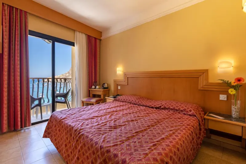 Chambre avec un grand lit et un balcon donnant sur la mer.