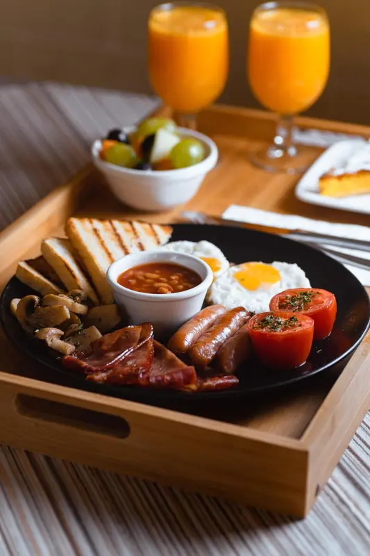 Un plateau de petit-déjeuner copieux avec des œufs, des saucisses, du bacon et des fruits.
