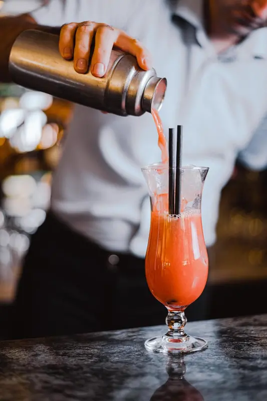 Un barman prépare un cocktail coloré au comptoir.
