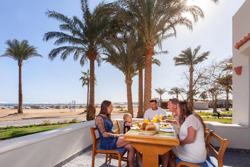 Une famille prend son petit-déjeuner à une table en extérieur face à la mer.