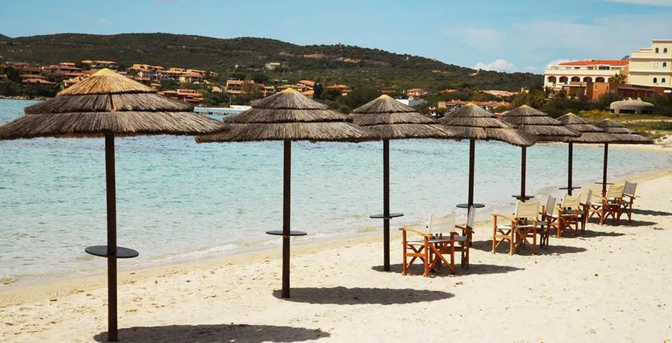 Parasols en chaume et chaises longues sur une plage de sable fin.