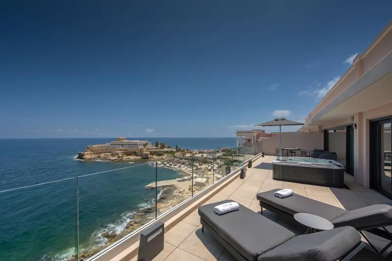 Terrasse avec transats et jacuzzi offrant une vue sur la mer et le littoral.