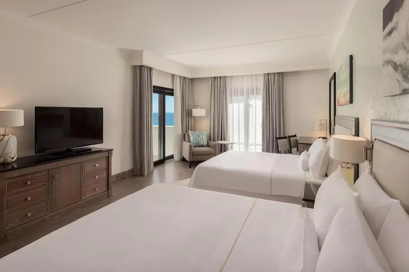 Une chambre lumineuse avec deux lits et un fauteuil près d'une baie vitrée.