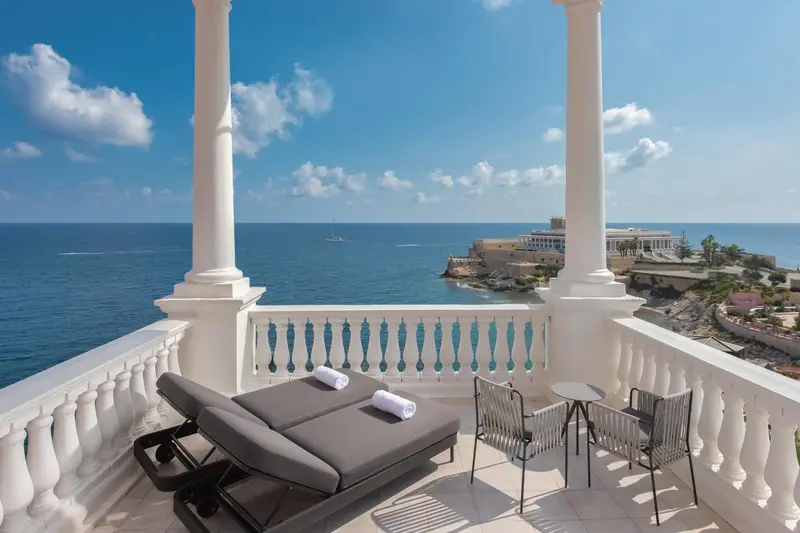 Terrasse avec transats et vue sur la mer et un promontoire rocheux.