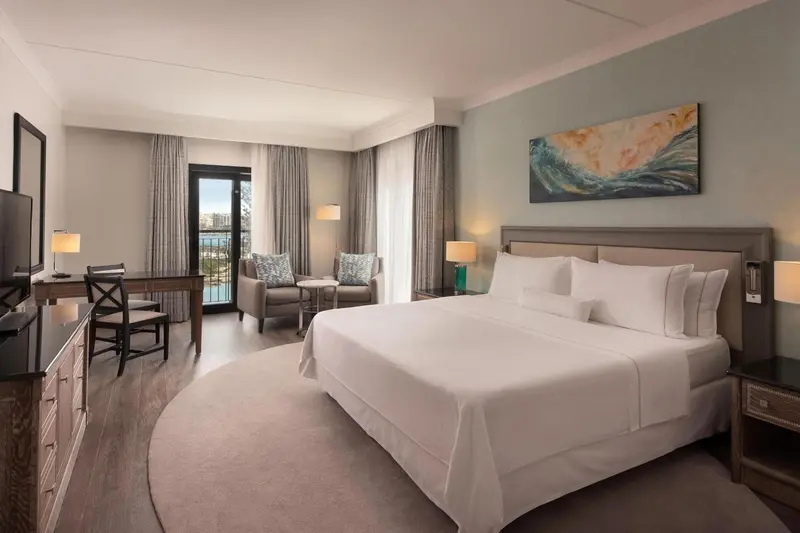 Chambre lumineuse avec un grand lit et un coin salon près d'une baie vitrée.