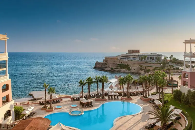 Vue aérienne d'une piscine d'hôtel surplombant la mer et une côte rocheuse.