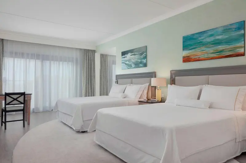 Deux lits simples dans une chambre lumineuse avec des rideaux blancs.