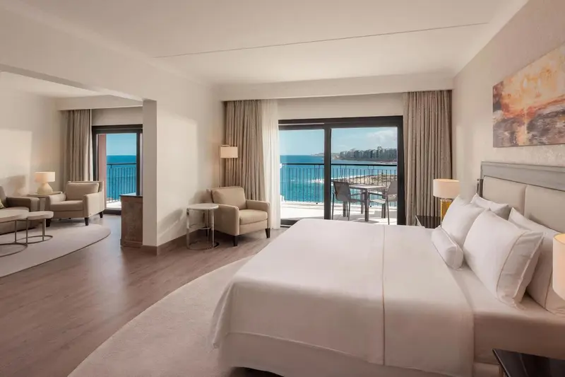 Une chambre lumineuse avec un grand lit et un coin salon donnant sur la mer.