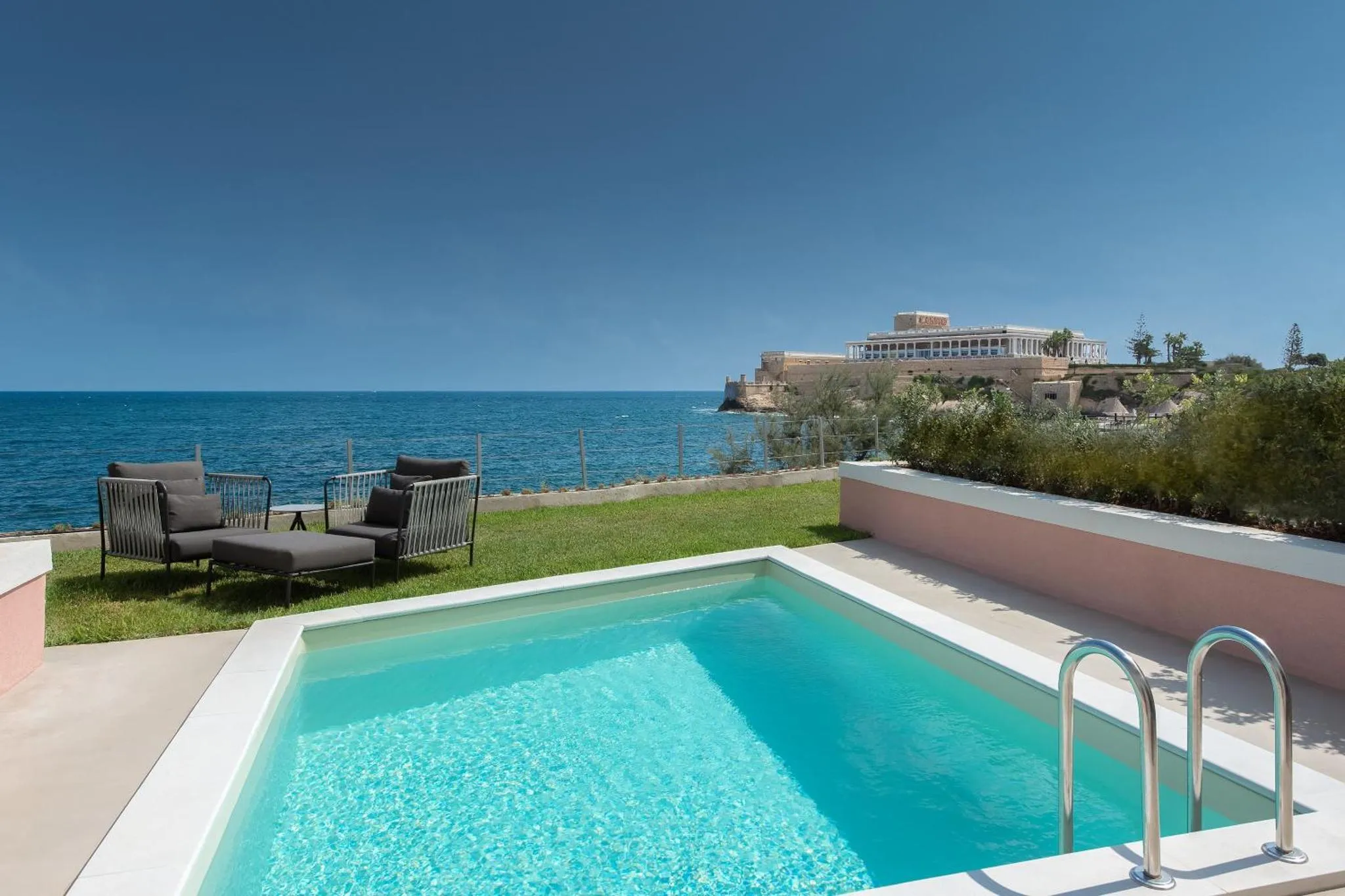 Petite piscine avec transats sur une terrasse ensoleillée face à la mer.