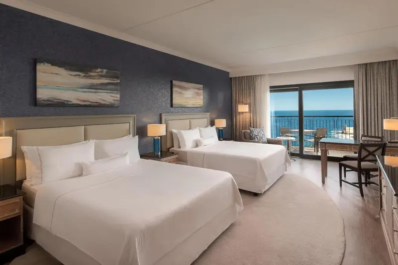 Chambre lumineuse avec deux lits et vue sur la mer.