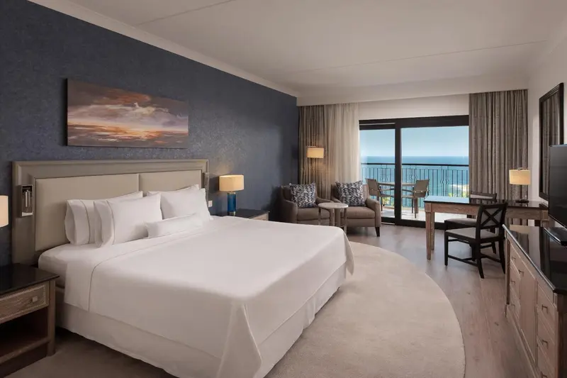 Une chambre lumineuse avec un grand lit et un espace salon donnant sur une vue mer.