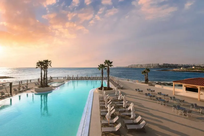 Une piscine à débordement surplombe la mer au coucher du soleil.