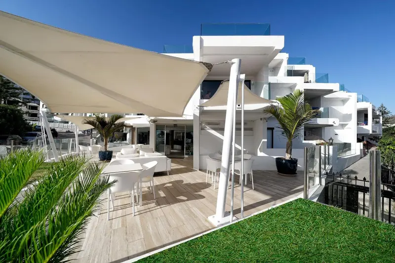 Terrasse ombragée avec mobilier blanc et végétation tropicale.