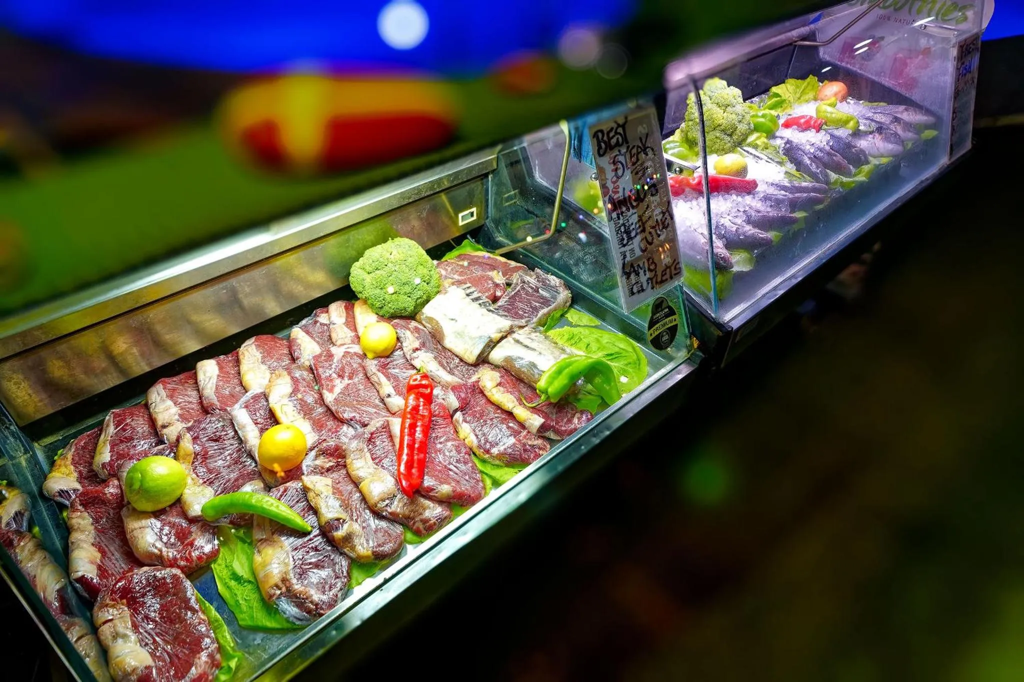 Présentation de morceaux de viande crue, garnis de légumes et d'épices dans une vitrine réfrigérée.
