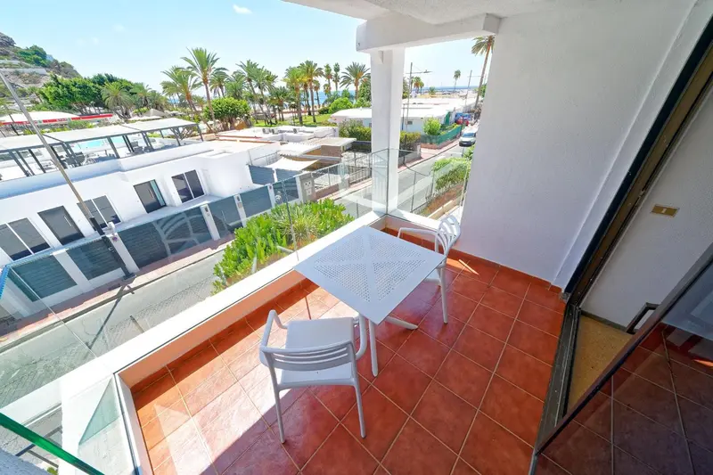 Une terrasse carrelée avec une table et des chaises blanches offre une vue sur la végétation et la mer.