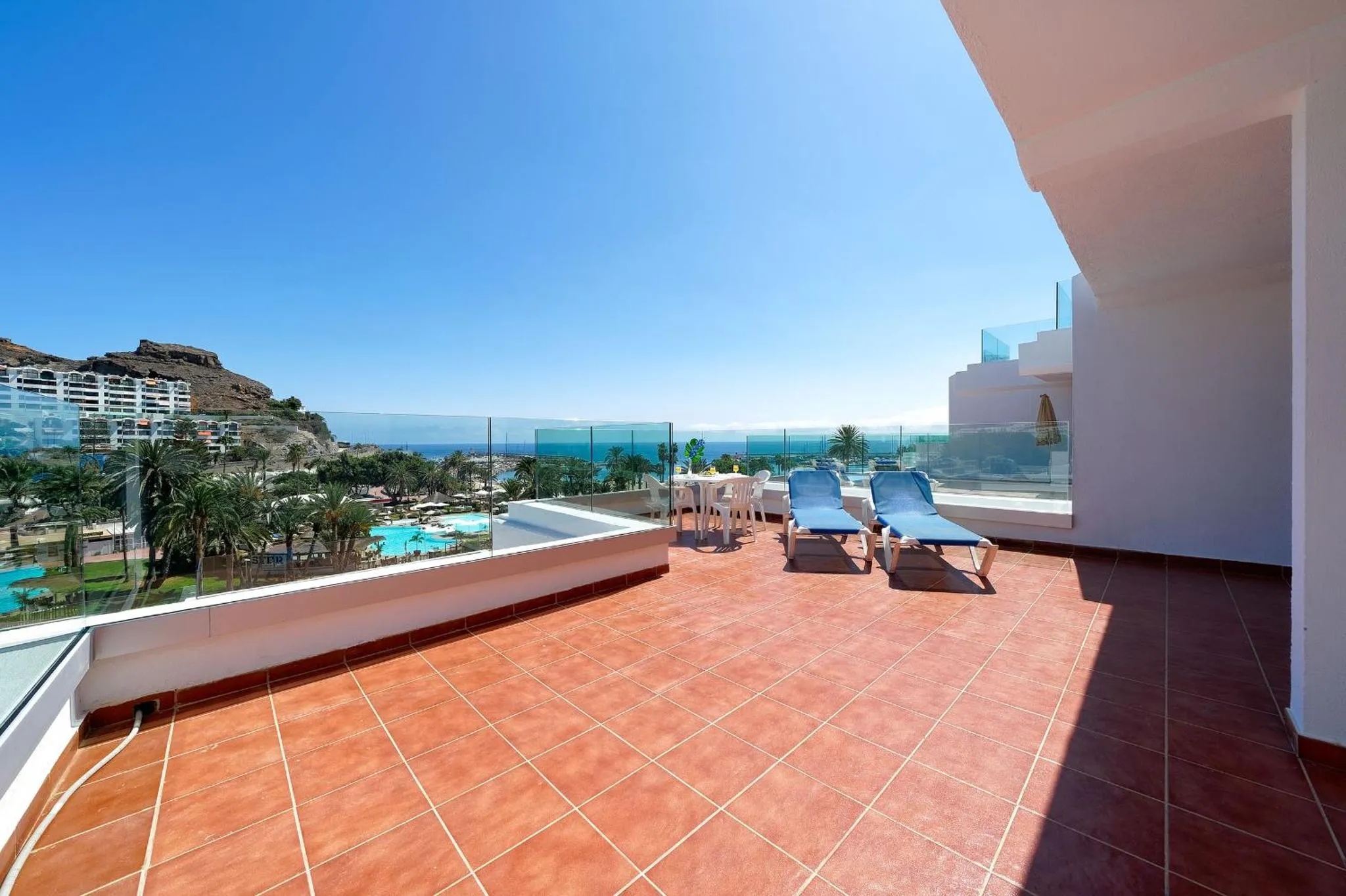 Terrasse carrelée avec transats et vue sur la mer et les montagnes.