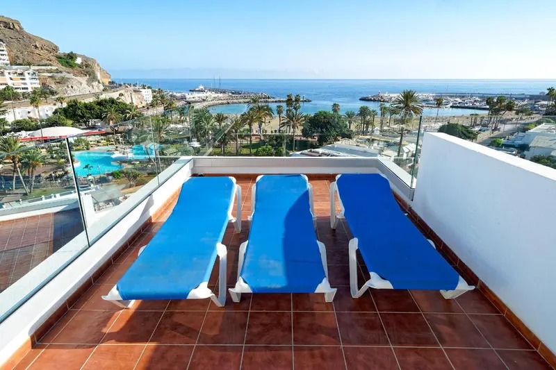 Transats bleus sur une terrasse carrelée avec vue sur la mer et la côte.