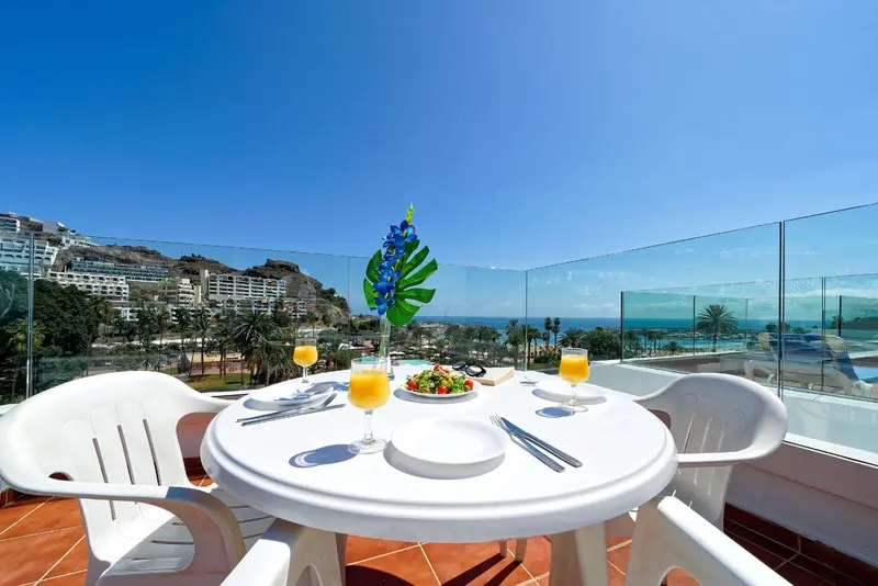 Une table blanche est dressée sur une terrasse avec vue sur la mer et les montagnes.