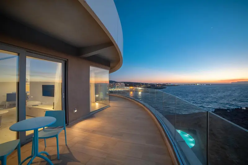 Terrasse avec mobilier bleu et vue sur la mer au coucher du soleil.