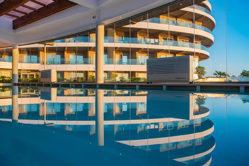 Bâtiment moderne avec de larges baies vitrées se reflétant dans une piscine calme.