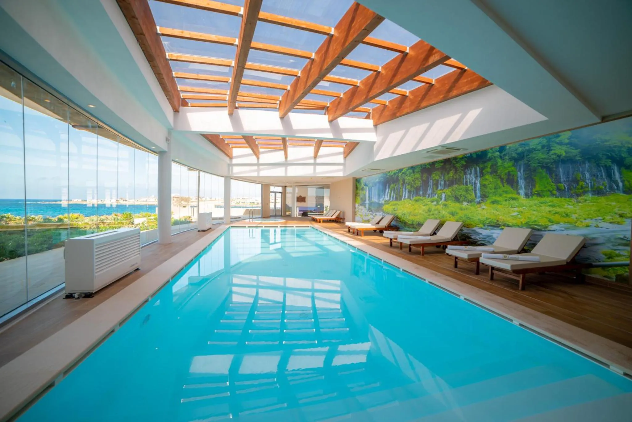Piscine intérieure lumineuse avec vue sur la mer et des transats.