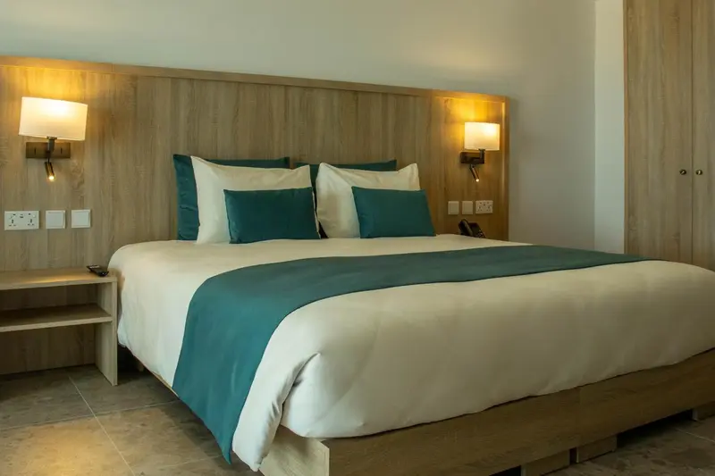 Une chambre lumineuse avec un grand lit recouvert d'une courtepointe turquoise et de coussins assortis.