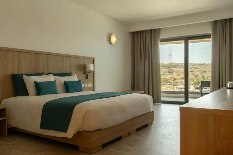 Une chambre lumineuse avec un grand lit et une vue sur un paysage aride.